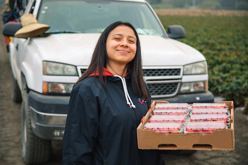 A young woman holding a case of strawberries
