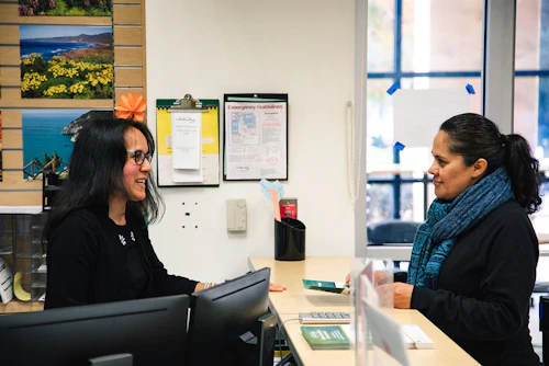 A student and an instructor are speaking at the office desk