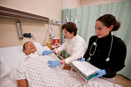 Student and instructor practicing patient care in a hospital bed