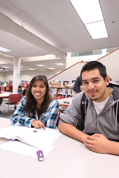 A male and a female student smiling while studying in the library