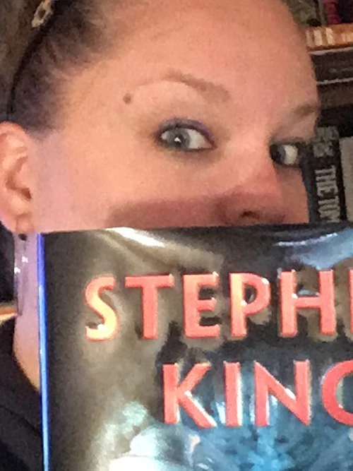Michaela asomándose desde detrás de un libro de Stephen King y Owen King.