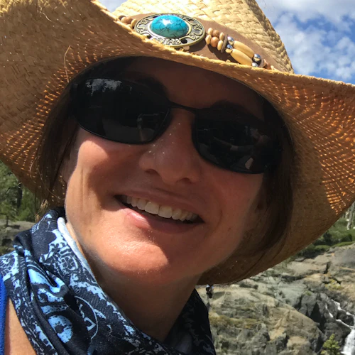 Sally smiling and wearing a wide brim straw hat, sunglasses and blue bandanna