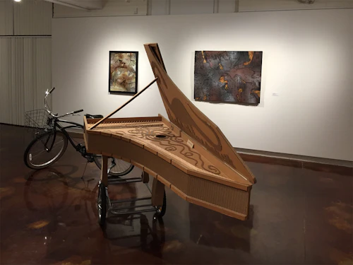 vista de instalación con arpa de cartón y pinturas de cartón en el fondo