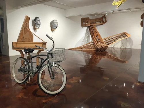 vista de instalación mostrando bicicleta que tira arpa de péndulo y avión kamikaze hecho de cartón estrellado