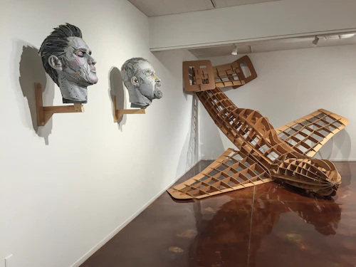 ver con un avión en el fondo y cabezas de cartón meticulosamente esculturadas en primer plano, muy alto en la pared