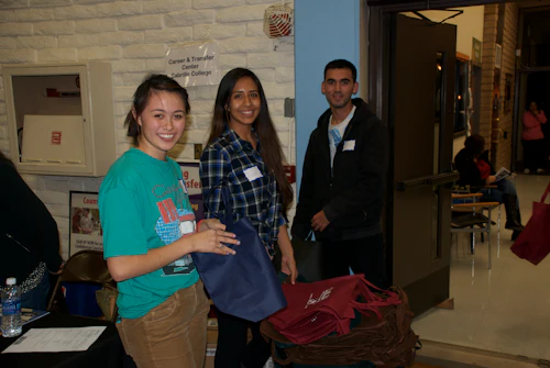 three smiling students in casual dress standing in the gym in front of a brick wall