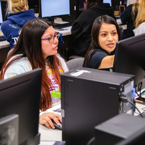 Dos estudiantes colaborando en trabajo de computadora