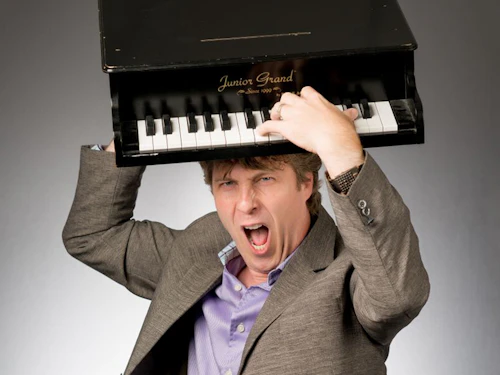 David Cutler con un piano de juguete en la cabeza y una expresión de estrella de rock en el rostro.