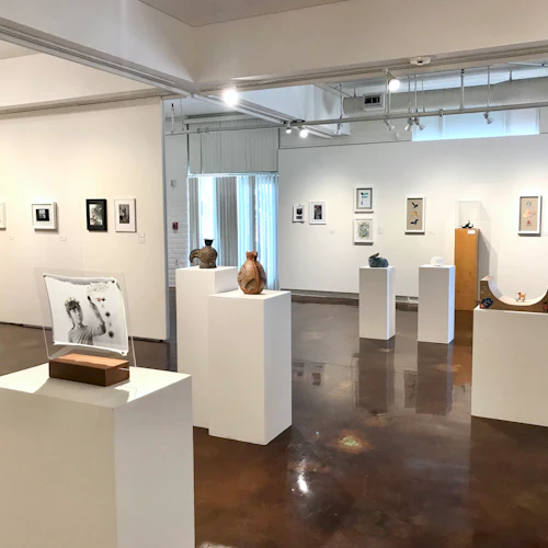 overview of gallery installation with artwork on pedestals in middle of room surrounded by artwork on walls