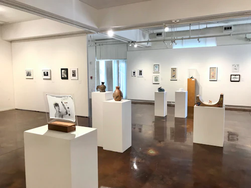 overview of gallery installation with artwork on pedestals in middle of room surrounded by artwork on walls