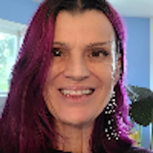 Sadie smiling in a blue room with plants; she has light skin and purplish hair, blue wall,