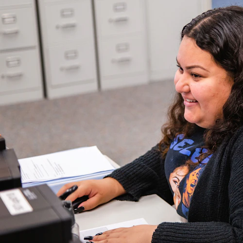 Estudiante trabajando en una computadora sonriendo.