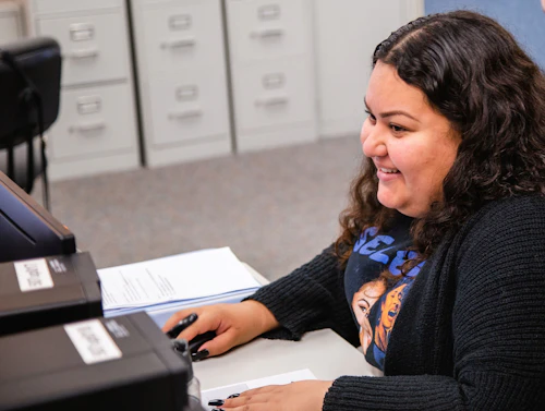 Estudiante trabajando en una computadora sonriendo.