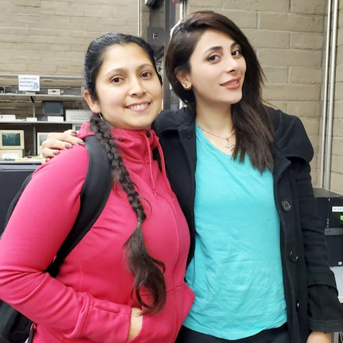Dos amigos parados en el laboratorio de computación con mochilas, sonriendo.
