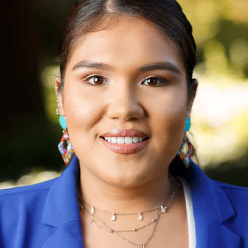 Alicia wearing a blue blazer with greenery in the background.
