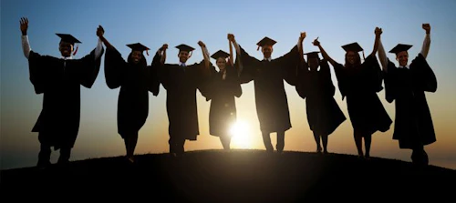 one row of students in graduation regalia holding raised hands with the sunrise in the background