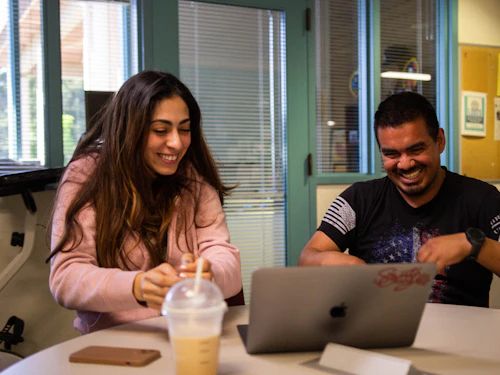 un hombre y una mujer sonríen mientras miran una laptop