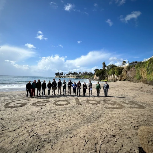 estudiantes en la playa frente a la palabra geología escrita en la arena