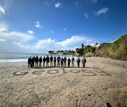 estudiantes en la playa frente a la palabra geología escrita en la arena
