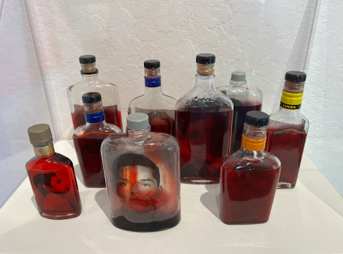 Victor Cartagena, botellas con líquido rojo y transferencias fotográficas de caras, instalación