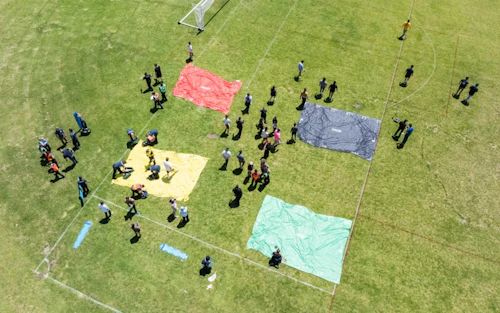 Vista aérea de personas paradas en un campo de fútbol con varias lonas de colores.