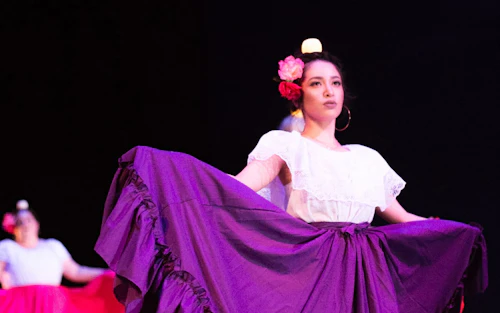 Bailarina con vestido morado en primer plano y una segunda detrás de ella y a la izquierda.