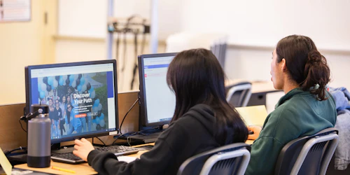Two female student sit at a computer designing a website.