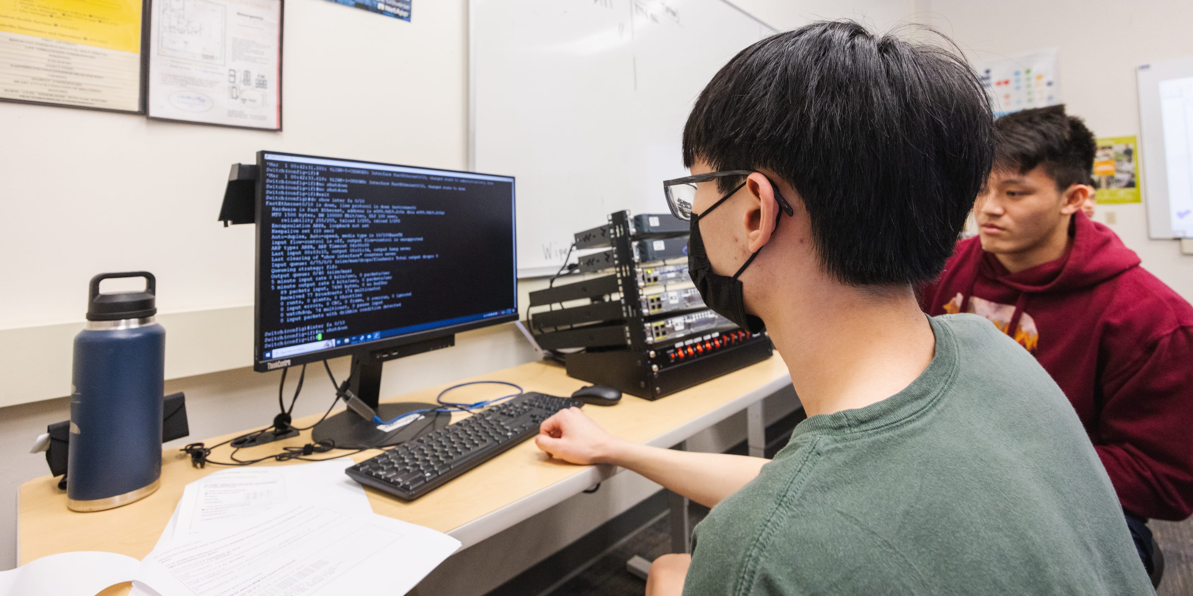 Two male students sit a computer writing code for a website.