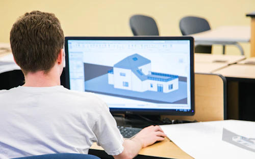 Un estudiante varón se sienta frente a una computadora diseñando una casa.