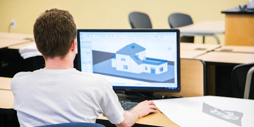 A male student sits at a computer designing a house.