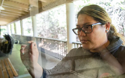 Una estudiante recoge huellas dactilares en una puerta de vidrio transparente.