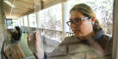 A female student dusts for fingerprints on a clear glass door