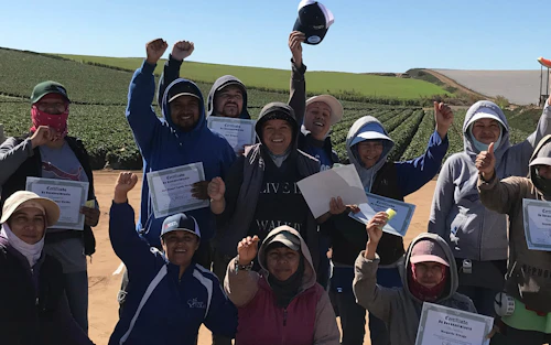 Un grupo de recolectores de fresas y un organizador laboral sostienen certificados.