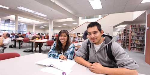A female and male student sit at a desk in a library