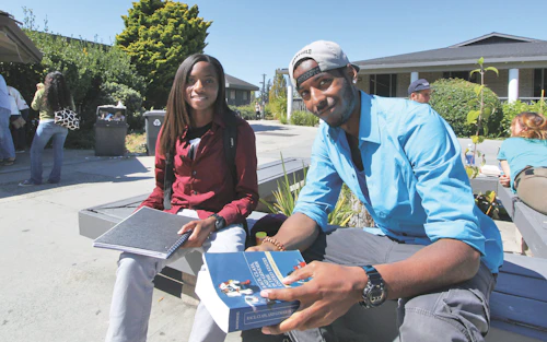 Una estudiante y un estudiante están sentados en un banco en el cuadrante superior del campus de Cabrillo College.