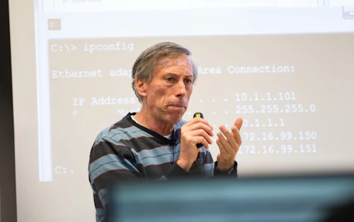 Un profesor de ciencias de la computación da una conferencia frente a una pantalla de proyector con código de computadora.