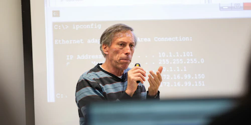 A computer science professor lectures in front of a projector screen with computer code