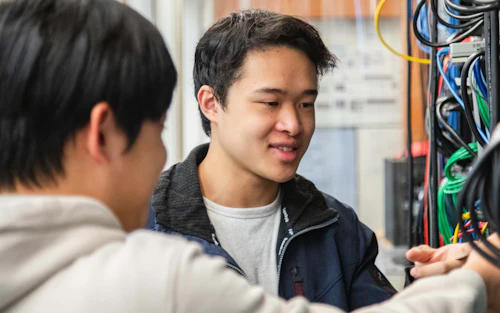Dos estudiantes varones examinan un rack de servidores.