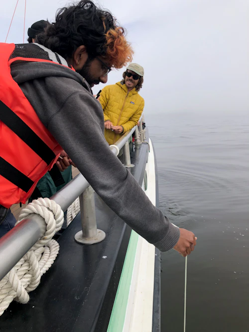 Students smiling, lowering oceanographic equipment over the side of a ship