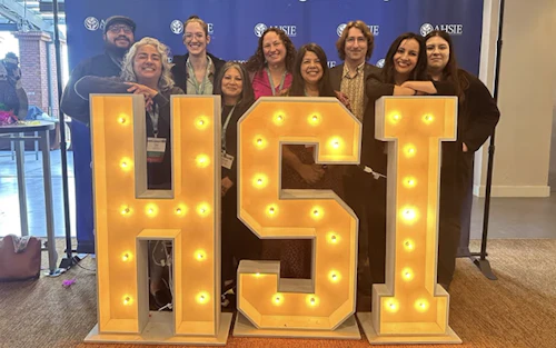 a group poses for a photo behind large letters HSI