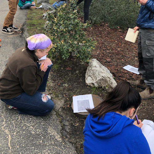 students sitting and standing outside, taking notes