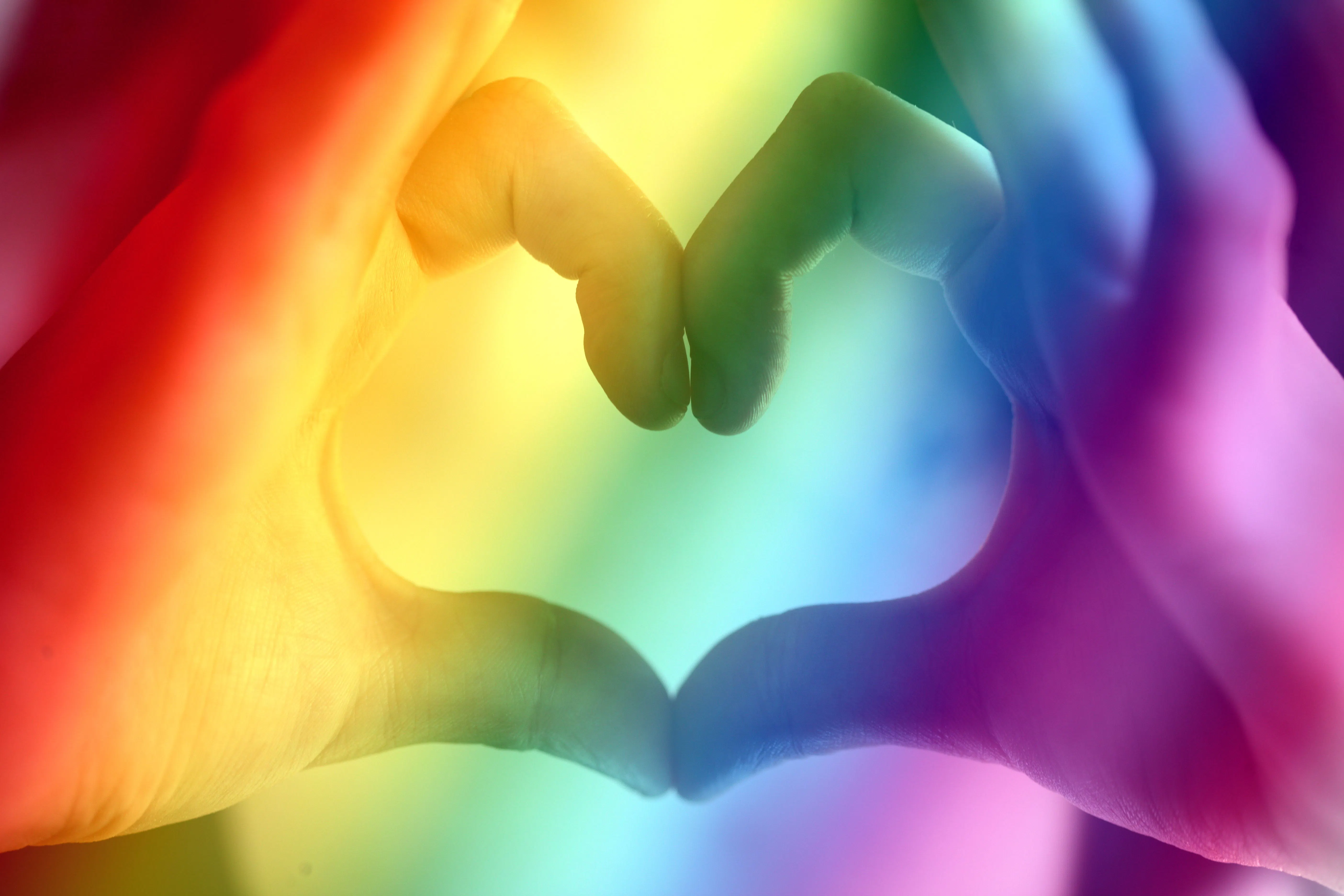 A hand making a heart with a rainbow overlay.