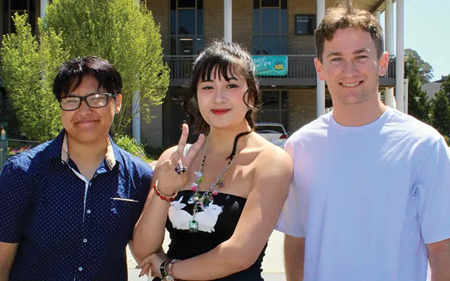 three students on campus smile for a photo together
