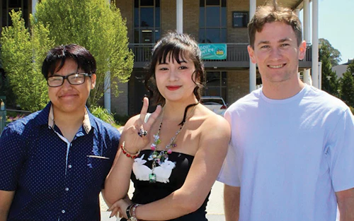 three students on campus smile for a photo together