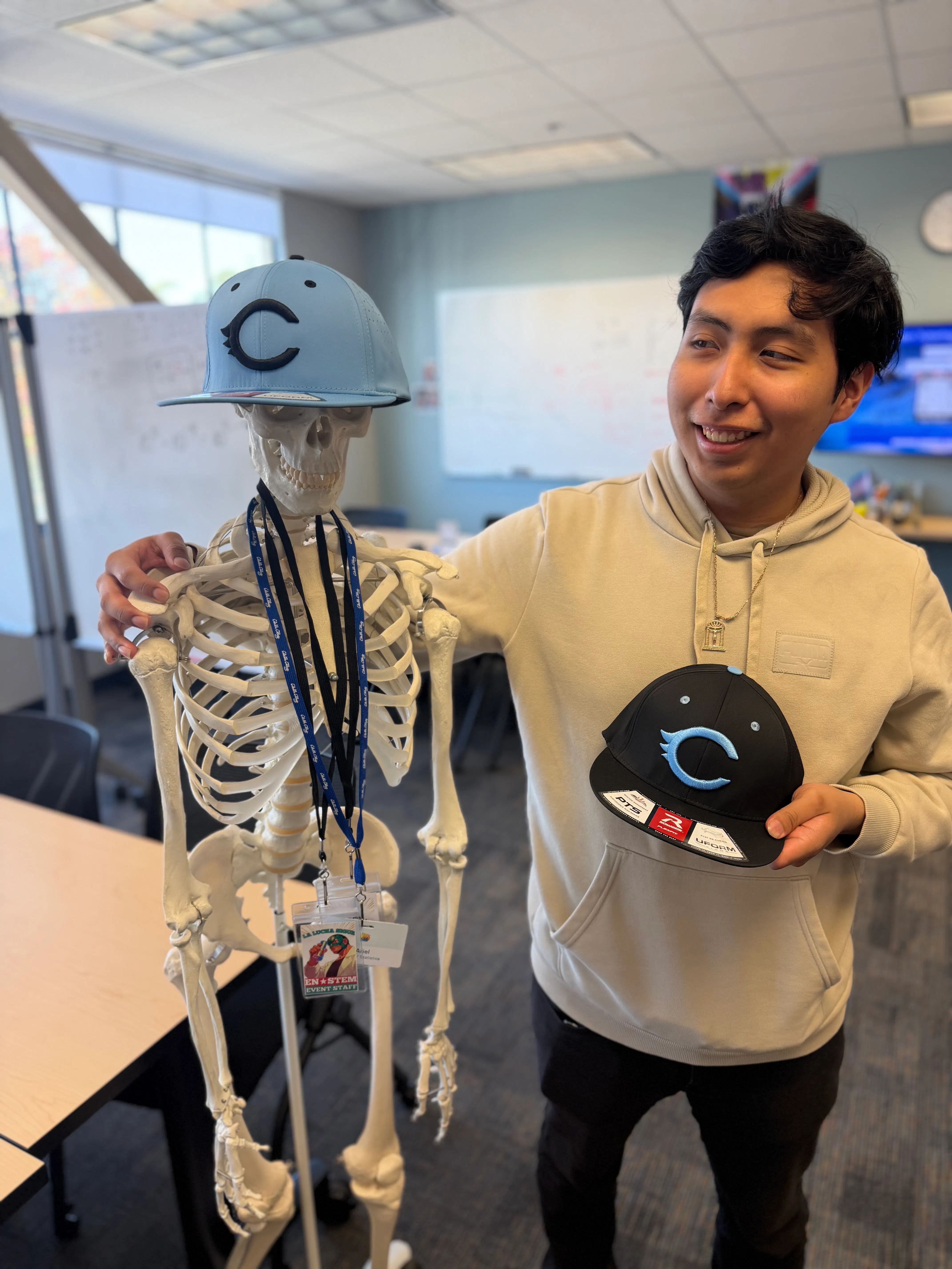a young man stands next to a skeleton model