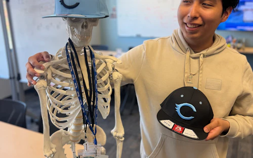 a young man stands next to a skeleton model