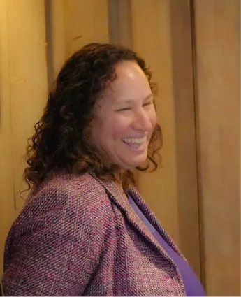 Mixed Race, curly hair Dean smiling in purple top and pink plaid blazer.