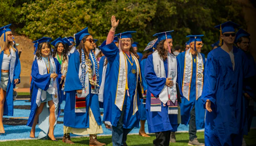 Cabrillo students in blue robes walk across the stage at the 2026 graduation