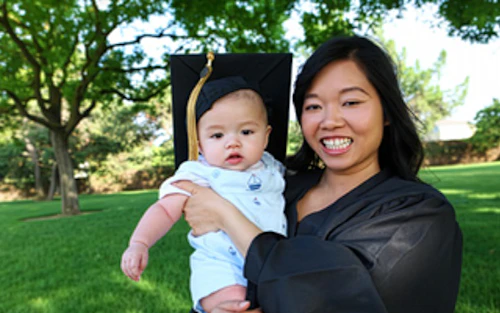 a Cabrillo student wearing a graduation gown holds her baby